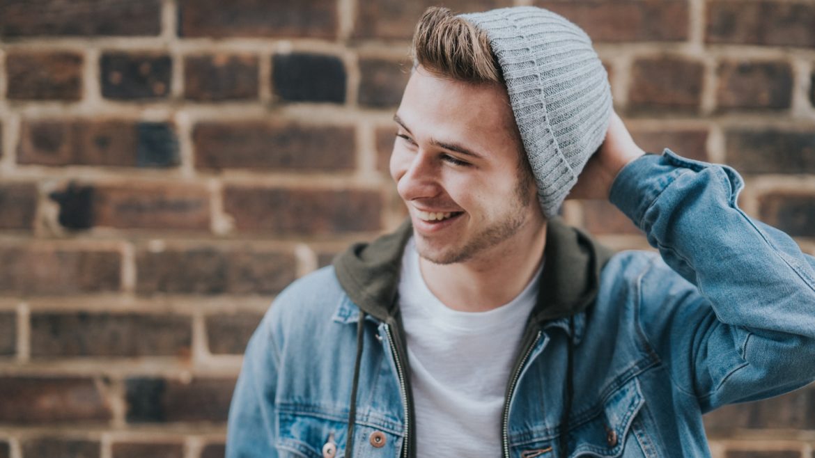 man holding the back of his head while smiling near brick wall